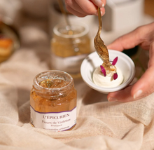 Load image into Gallery viewer, Person spooning violet confit from a jar labeled 'L'Epicurien' onto a dish with whipped cream and flowers.