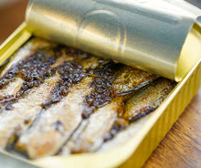 Load image into Gallery viewer, Close-up of open tin of Fangst sea sprat (Nordic sardine) with heather and chamomile.