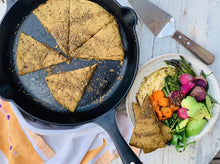 Load image into Gallery viewer, Maskal teff flat bread, in cast iron skillet, alongside salad of fresh veggies and hummus.