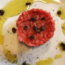 Load image into Gallery viewer, Fried salted capers on round patty of steak tartar with olive oil and cracked pepper on white plate.