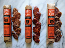 Load image into Gallery viewer, All three Fatted Calf single breed salamis in original packaging, with sliced product next to it, on marble table (Napa, California).