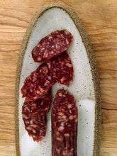 Load image into Gallery viewer, Fatted Calf artisan Red Wattle salami sliced on an off white stoneware oval plate, on wood table.
