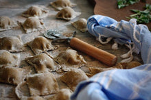 Load image into Gallery viewer, Handmade Maskal teff raviolis, blue and white linen towel, and cutting tool on cutting board.