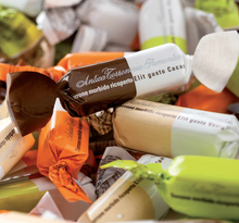 Load image into Gallery viewer, A close-up pile of wrapped chocolates, with one prominent dark brown wrapper reading 'Antica Terrazzio Promontes' and other wrappers in orange, beige, and light green visible around it.
