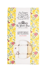 Load image into Gallery viewer, Le Petit Luxe Assortiment de Calissons Les Fruits packaging, featuring a white central label with black script and illustration, bordered by yellow floral patterns with pink and blue blossoms, and a clear window showing white calissons with dark berry centers.
