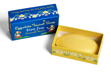 Pretty blue box of Eiwit Zeep eggwhite soap with chamomile flowers and Swiss girls in colorful dresses on the left and right side.  Oval embossed bar of soap next to box.  White background.