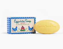 Load image into Gallery viewer, A yellow oval bar of Eggwhite Facial Soap next to its blue and white illustrated box labeled 'Eggwhite Soap made with CHAMOMILE' on a clean white background.  New packaging.
