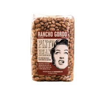 Load image into Gallery viewer, A bag of Rancho Gordo Pinto Bean coffee beans sits on a piece of burlap fabric against a rustic wooden background.
