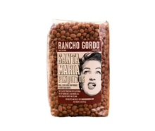 Load image into Gallery viewer, A clear plastic bag of Rancho Gordo Santa Maria Pinotillos beans sits on a piece of burlap over a wooden surface, with a rustic, blurred brown background.
