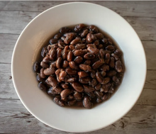 Load image into Gallery viewer, Cooked black beans in a light brown sauce, served in a white ceramic bowl on a rustic gray wooden table.  Rancho Gordo Rio Zapi Dried Beans
