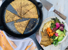Load image into Gallery viewer, Teff flat bread, in cast iron skillet, alongside salad of fresh veggies and hummus.

