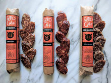 Load image into Gallery viewer, Fatted Calf Salami -all 3 single breed flavors.  Full size salami wrapped in kraft paper with red and black label, next to sliced salami of the same type.
