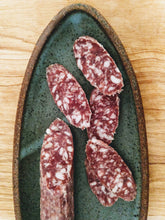 Load image into Gallery viewer, Fatted Calf Berkshire salami sliced on green stoneware oval plate, on wood table.
