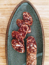 Load image into Gallery viewer, Fatted Calf Duroc Salami Sliced on green stoneware oval platter, on wood table.
