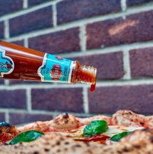 Load image into Gallery viewer, Firelli Italian Hot Sauce Bottle being pour on pizza, against brick background.
