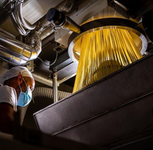 Load image into Gallery viewer, Spaghetti pasta being extruded in factory with masked staff overlooking production
