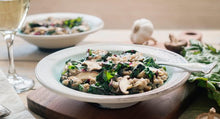 Load image into Gallery viewer, Teff grain kale and mushroom salad, served in white bowls, on wood cutting board, with garlic, mushrooms and greens in background.
